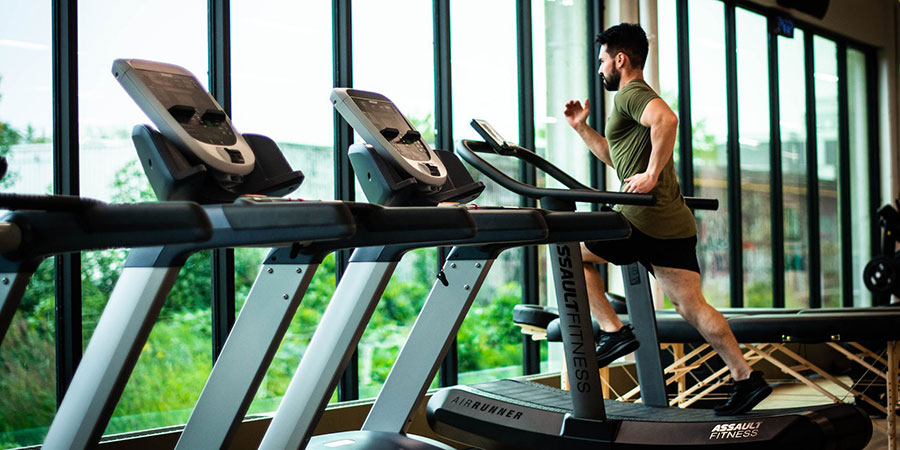a man running on a treadmill at the gym with several other treadmills and a floor to ceiling windows